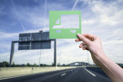 Hand holds green logistics truck symbol against highway