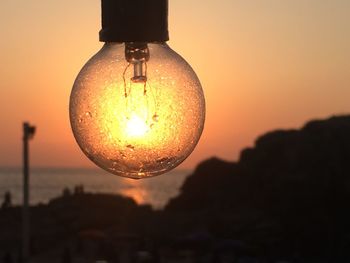 Close-up of illuminated light bulb against sky during sunset