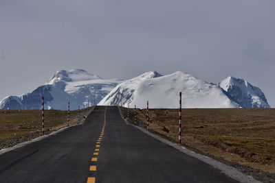 Road leading towards snowcapped mountains against sky