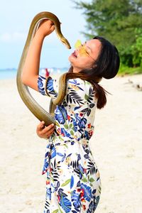 Young woman holding snake while standing at beach