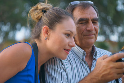 Young woman looking at camera while man photographing outdoors