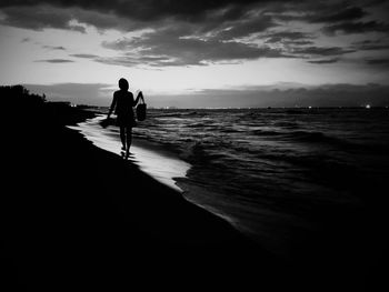 Woman walking on shore at beach during sunset