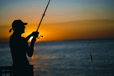 Silhouette man fishing in sea against sky during sunset