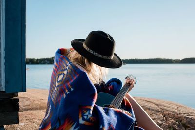 Woman sat playing the guitar at the beach wrapped in pendleton