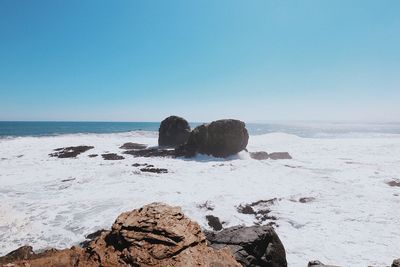 Rocks on beach against clear blue sky