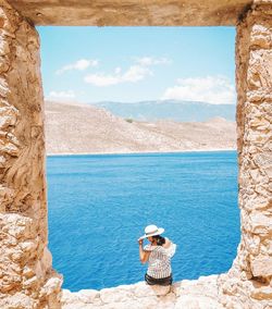 Rear view of woman sitting on rock formation against sea