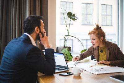 Confident female illustrator discussing over drawing with male colleague at table in office