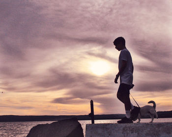 Side view of man standing by sea against sky during sunset