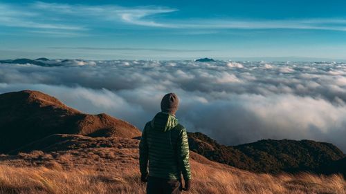 Rear view of man standing on mountain against sky