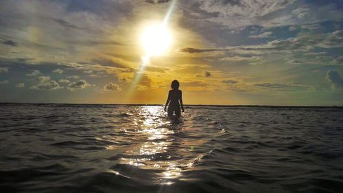 Silhouette person in sea against sky during sunset