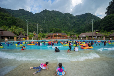 People enjoying in swimming pool against mountains