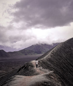 Man walking on mountain against cloudy sky