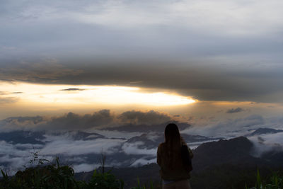 Rear view of woman standing against sky during sunset