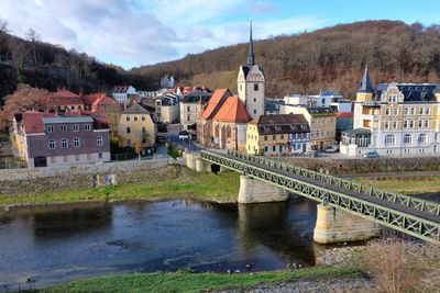 Bridge over river by buildings against sky