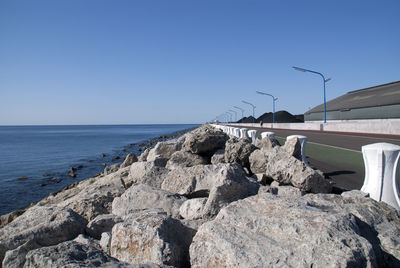 Rocks by sea against clear blue sky