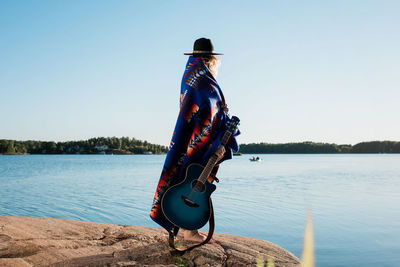 Woman stood wrapped in a pendleton blanket holding a guitar