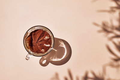 Traditional italian dessert tiramisu in a glass cup on a light beige background with leaves shadows