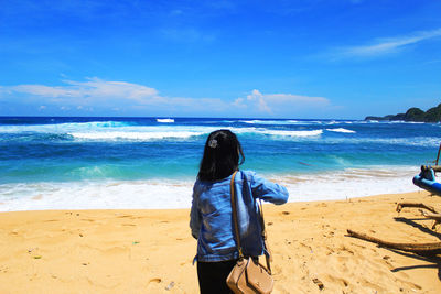 Rear view of man standing on beach against blue sky