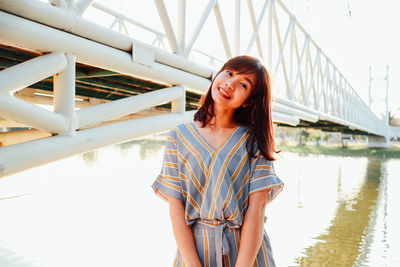 Portrait of smiling young woman standing against bridge and lake