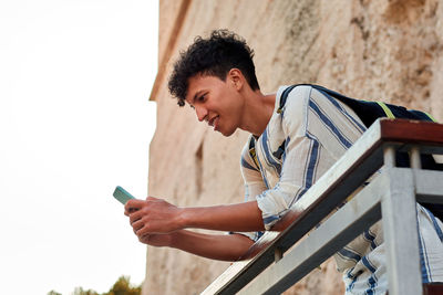 Young man with afro hair is using his smartphone outdoors