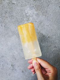 Cropped image of hand holding ice stick against concrete wall