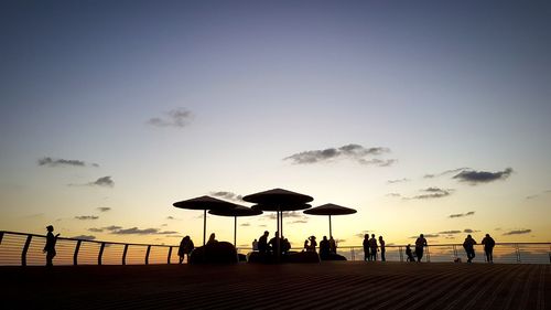 Silhouette people at beach against sky during sunset