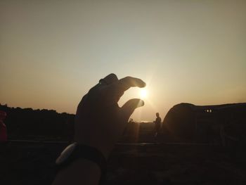 Silhouette hand against sky during sunset