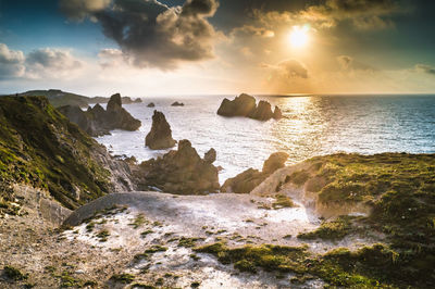 Rocks in sea against sky during sunset