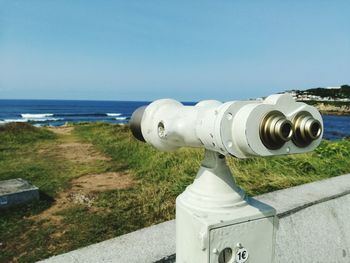 Coin-operated binoculars by sea against clear sky