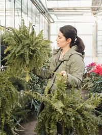 Pensive adult buyer touching green leaves and selecting to buy potted plant in modern greenhouse market