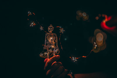 Close-up of hand holding illuminated lighting equipment against black background