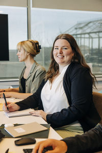 Portrait of smiling businesswoman sitting with colleagues at desk in coworking office