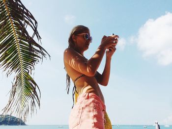 Low angle view of woman using phone at beach against sky