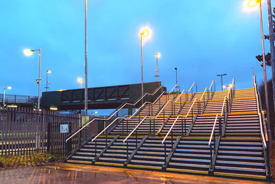 Illuminated street light by building against sky at dusk