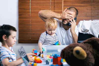 Portrait of father with head in hand while kids playing with toy on table at home