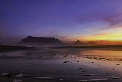 Scenic view of the sea during sunset, table mountain in background on a misty day, city lights shine