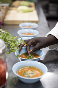 Cropped hand of woman garnishing soup on kitchen counter at restaurant kitchen