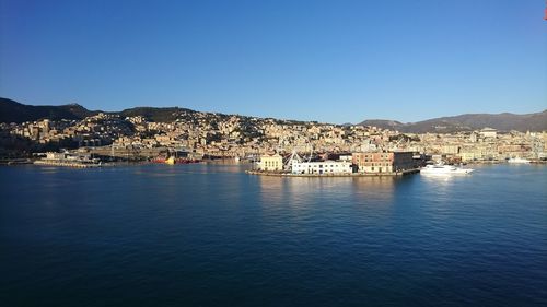 Scenic view of sea by townscape against clear blue sky