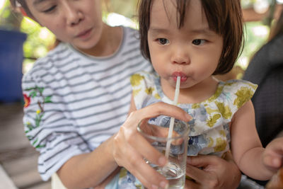 Woman feeding water to toddler daughter while sitting outdoors