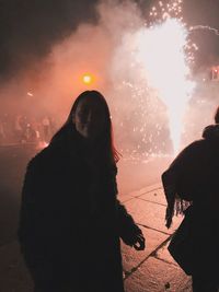 Woman standing by illuminated firework display at night