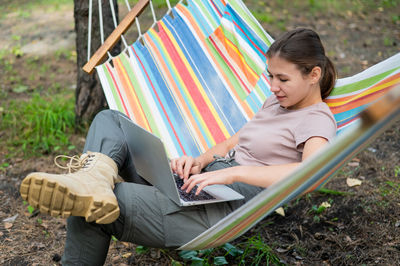 Woman working on laptop while sitting in a hammock in the forest. girl uses a wireless computer