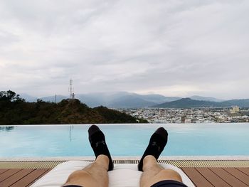 Low section of man relaxing in swimming pool against sky