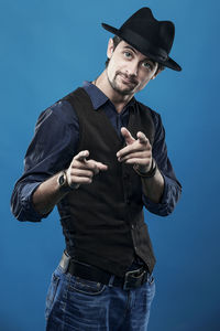 Portrait of fashionable young man pointing at you while standing against blue background