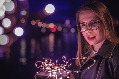 Close-up young woman holding illuminated string light at night