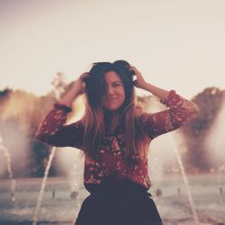 Smiling woman with hand in hair standing against fountain