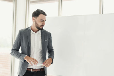 Businessman looking away while standing by whiteboard in office