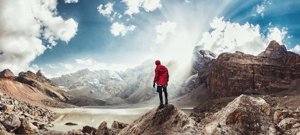 Rear view of man looking at mountains while standing on rock against sky