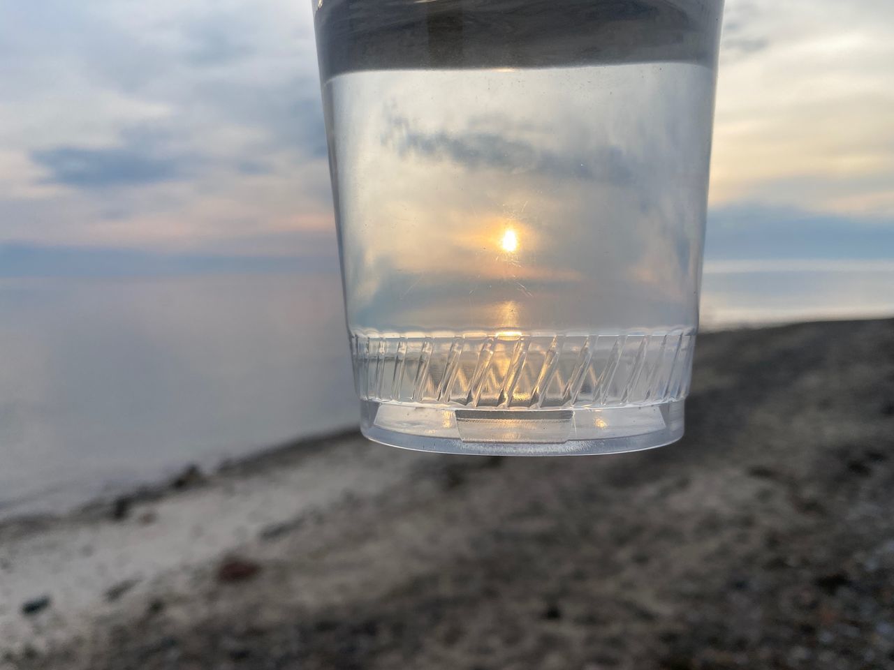 cloud, light, sky, water, nature, lighting, glass, single object, blue, no people, transparent, focus on foreground, reflection, sea, close-up, outdoors, land, white, sunset, drinking glass, beach, sand, environment, incandescent light bulb, dusk