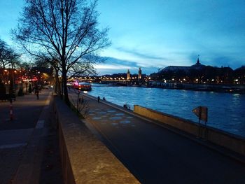 Illuminated city by river against sky