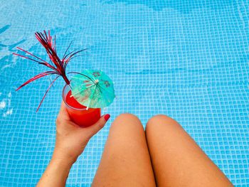 Midsection of woman holding drink while sitting by swimming pool